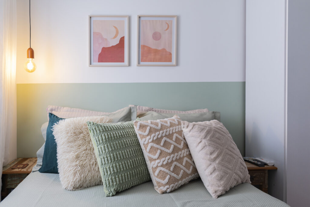 Quarto com cama escandinava em tons pastel e pequenos quadros decorativos na parede branca. 