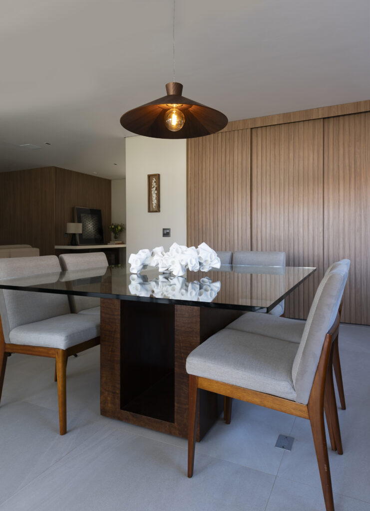 Sala de jantar com mesa de vidro, cadeiras estofadas e paredes de madeira clara. 