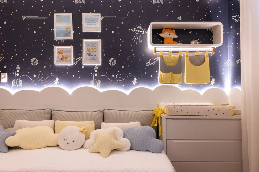 <img src="quarto-infantil-espaco-fofo.webp" alt="Quarto infantil decorado com tema espacial, incluindo almofadas de nuvem e estrela, parede escura com estrelas e foguetes, e prateleira com brinquedos.">