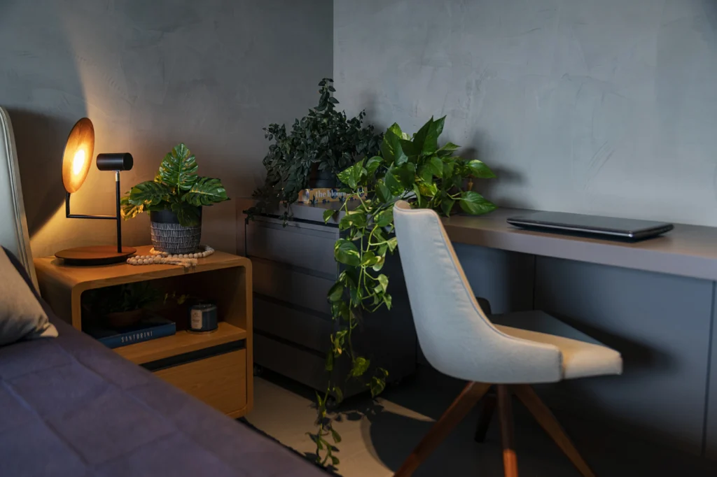 <img src="quarto-moderno-com-plantas.webp" alt="Ambiente de quarto moderno com plantas decorativas e uma mesa de trabalho. O espaço é iluminado por uma lâmpada e apresenta uma decoração minimalista.">