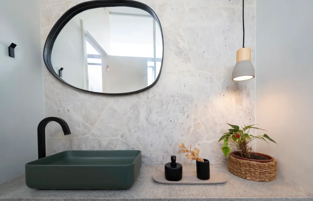 <img src="banheiro-moderno-com-pia-verde.webp" alt="Ambiente de banheiro moderno com pia verde, espelho oval, iluminação suave e elementos decorativos como plantas e acessórios em preto.">