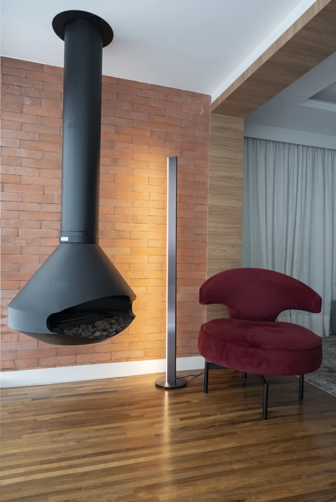 <img src="sala-moderno-lareira-suspensa-poltrona-vermelha.webp" alt="Imagem de uma sala moderna com uma lareira suspensa preta, uma luminária de pé e uma poltrona vermelha em ambiente aconchegante e elegante.">