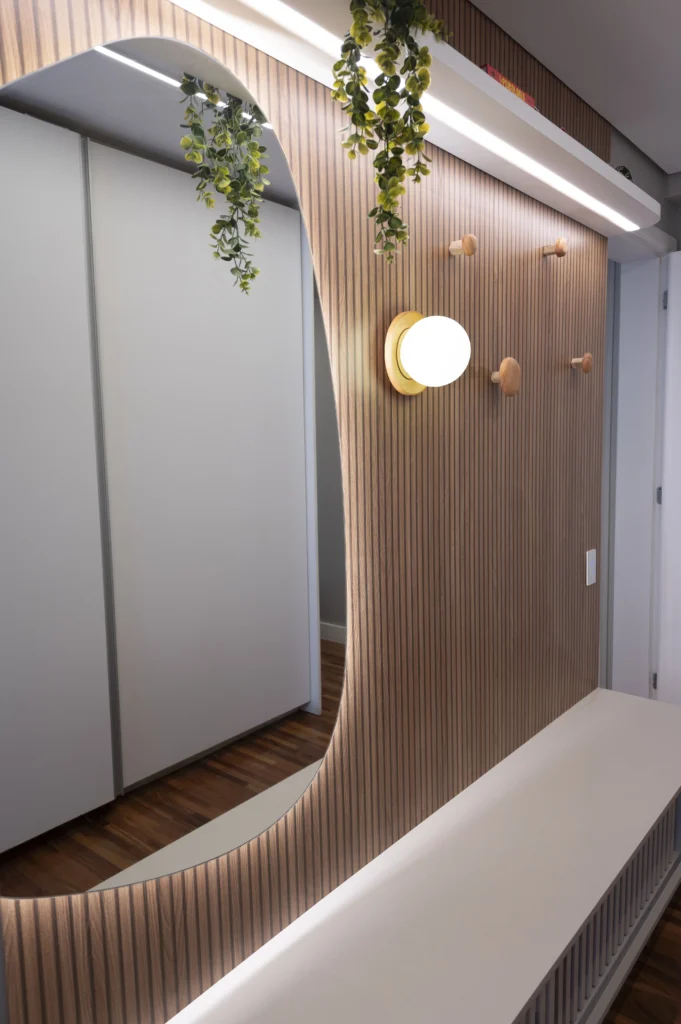 <img src="decoracao-interna-parede-madeira-espelho-iluminacao-plantas-jpg.webp" alt="Design de interior com parede de madeira, espelho decorativo, iluminação moderna e plantas penduradas, criando um ambiente aconchegante e elegante.">