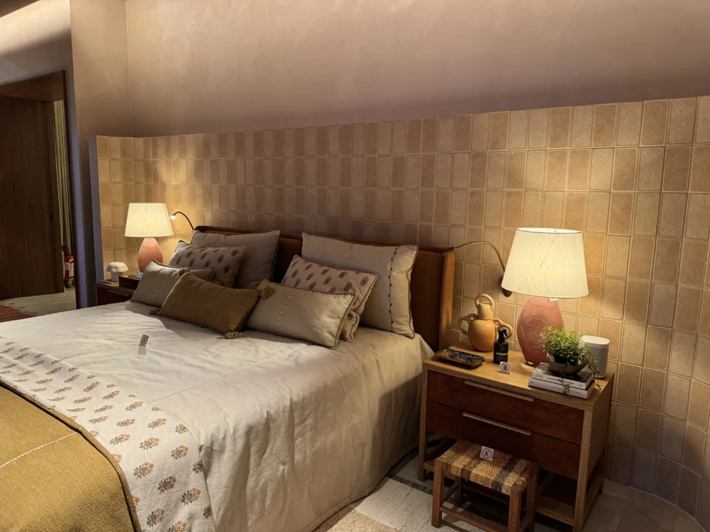 <img src="quarto-cama-de-casal-com-abajur-e-almofadas-aconchegante.webp" alt="Imagem de uma cama de casal com almofadas decorativas, ao lado de uma mesa de cabeceira com abajur, em um quarto bem decorado e aconchegante.">