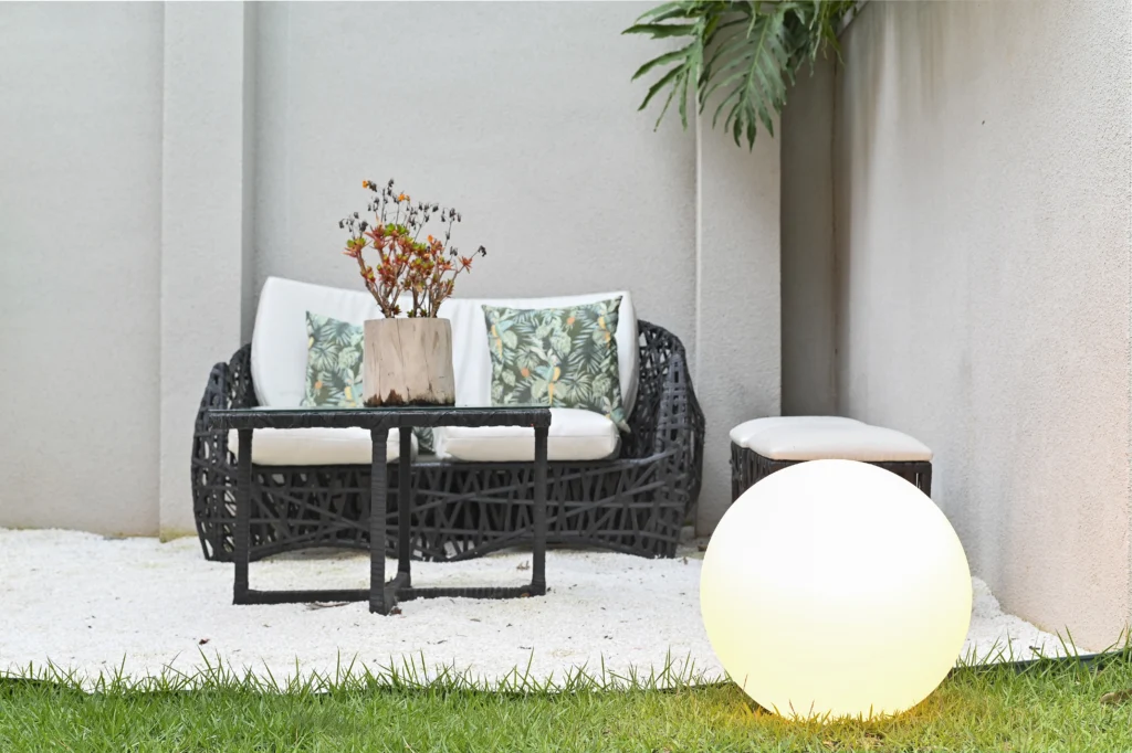 <img src="espaco-ao-ar-livre-com-moveis-de-varanda-e-luminaria-de-esfera.webp" alt="Área externa com mobiliário de varanda, incluindo sofá de fibra sintética, mesa de centro, uma luminária em formato de esfera e plantas decorativas. Ideal para criar um espaço acolhedor ao ar livre.">