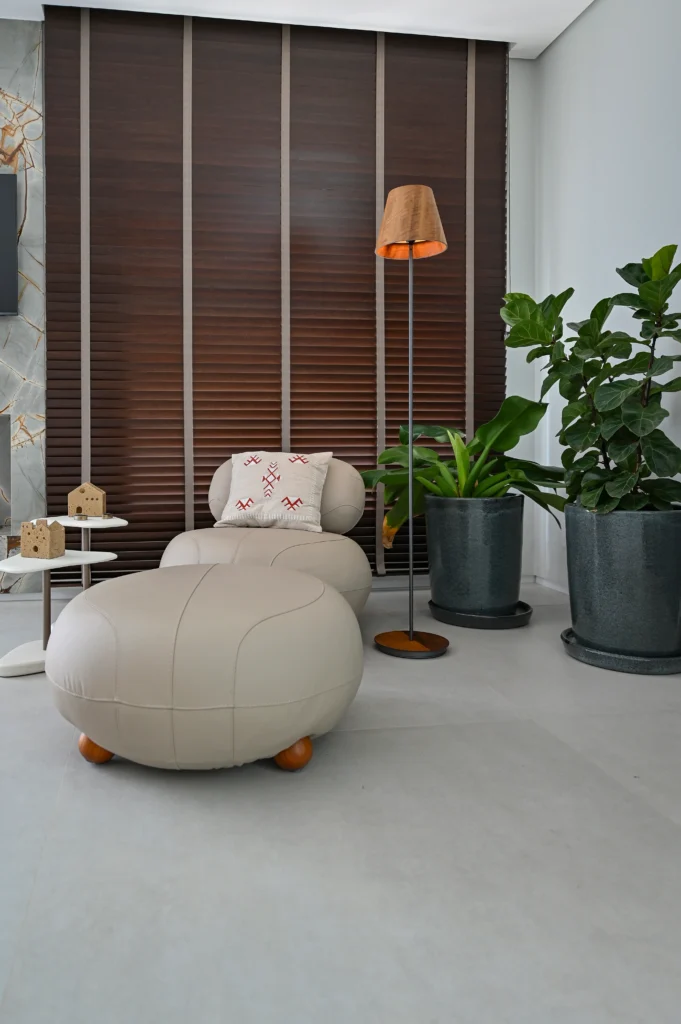 <img src="sala-de-estar-moderna-com-plantas-e-luminaria-de-piso.webp" alt="Sala de estar moderna com poltrona branca de design minimalista, plantas verdes em vasos cinza, luminária de piso e painel de madeira na parede, criando um ambiente aconchegante e elegante.">