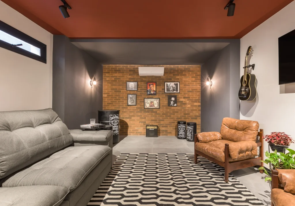 <img src="sala-de-estar-moderna-com-instrumentos-musicais.webp" alt="Sala de estar moderna com sofá cinza, poltrona de couro marrom, parede de tijolos expostos decorada com quadros, guitarra pendurada na parede, tapete geométrico preto e branco e instrumentos musicais no fundo.">