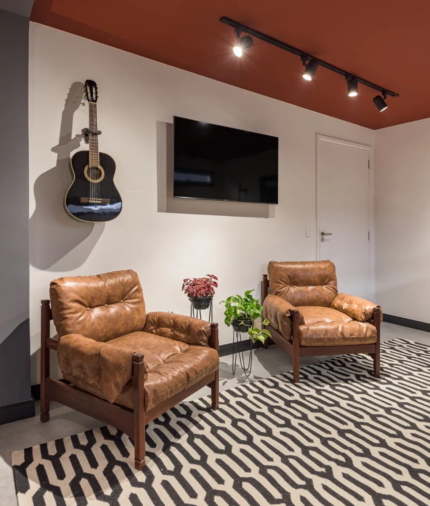 <img src="sala-de-estar-modernaconforto-inspiracao.webp" alt="Sala de estar moderna com duas poltronas de couro marrom, televisão de tela plana na parede, violão pendurado, plantas decorativas e iluminação direcionada.">