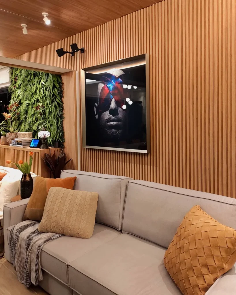<img src="decoracao-moderna-sala-estar-parede-madeira-quadro-rosto-estilo.webp" alt="Decoração moderna de sala de estar com parede de madeira, quadro de rosto estilizado, sofá com almofadas, plantas verdes e iluminação aconchegante.">