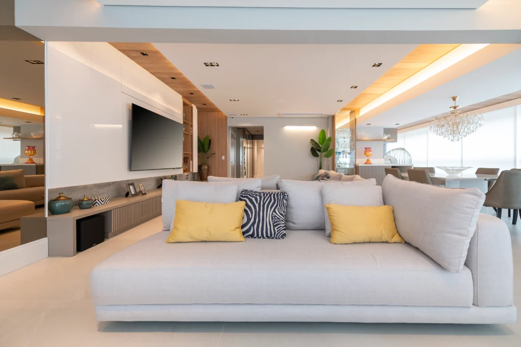 <img src="sala-estar-moderno-elegante-png.webp" alt="Imagem de uma sala de estar moderna e elegante com sofá branco, almofadas amarelas e decorativa azul e branca, iluminação suave e vista panorâmica.">