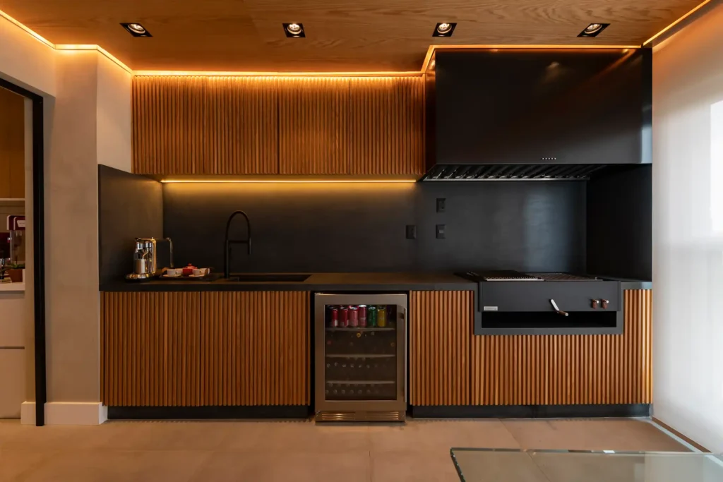<img src="cozinha-modernarevestimento-madeira-iluminacao-teto.webp" alt="Cozinha moderna com armários de madeira e iluminação de destaque em teto, equipada com cooktop, forno e lobby de bebidas.">