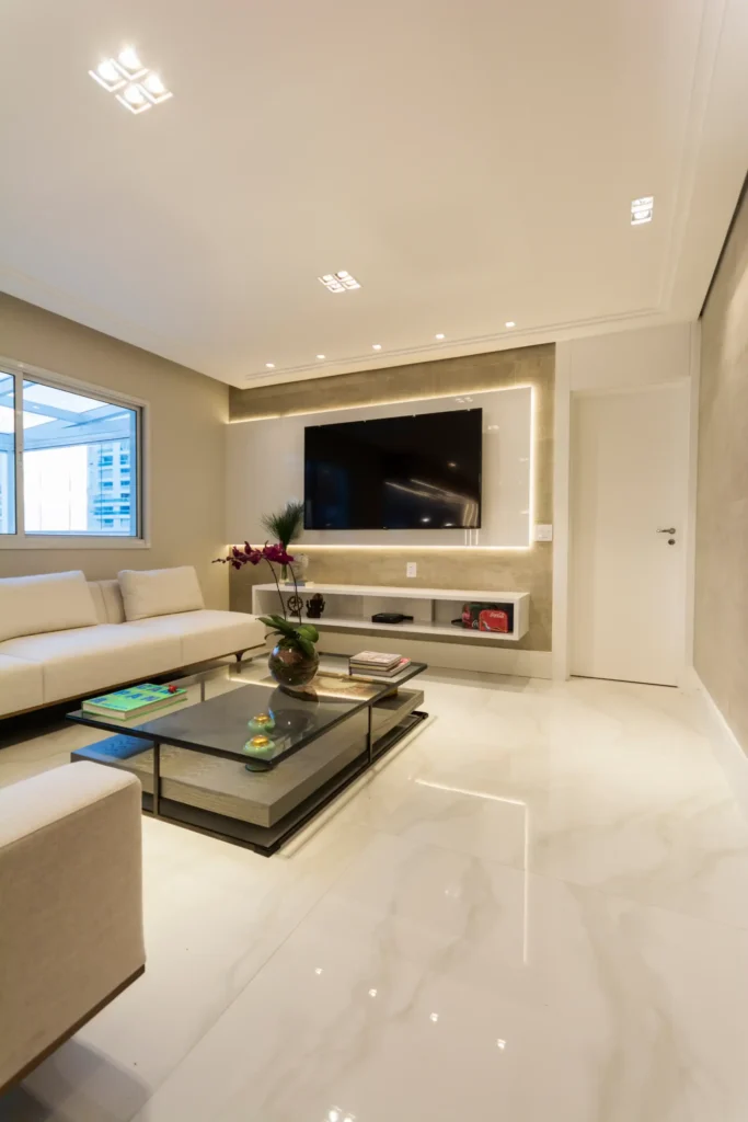 <img src="sala-de-estar-moderna-elegante.webp" alt="Imagem de uma sala de estar moderna com sofá branco, TV de tela plana na parede com iluminação indireta, mesa de vidro com livros e decoração elegante.">