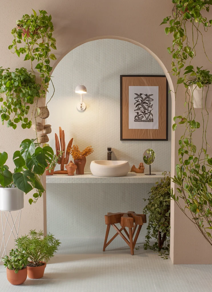 <img src="decoracao-de-banheiro-verde-e-moderna.webp" alt="Interior de banheiro com decoração moderna e plantas verdes, incluindo vasos de cerâmica, quadro de arte na parede e iluminação suave.">