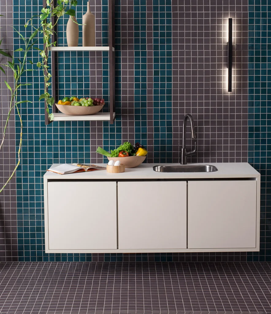 <img src="cozinha-moderna-com-azulejos-azuis-e-bancada-branca-jpg.webp" alt="Cozinha moderna com paredes de azulejos azuis, bancada branca com pia de inox e prateleira com frutas e vasos decorativos, ambiente organizado e contemporâneo.">