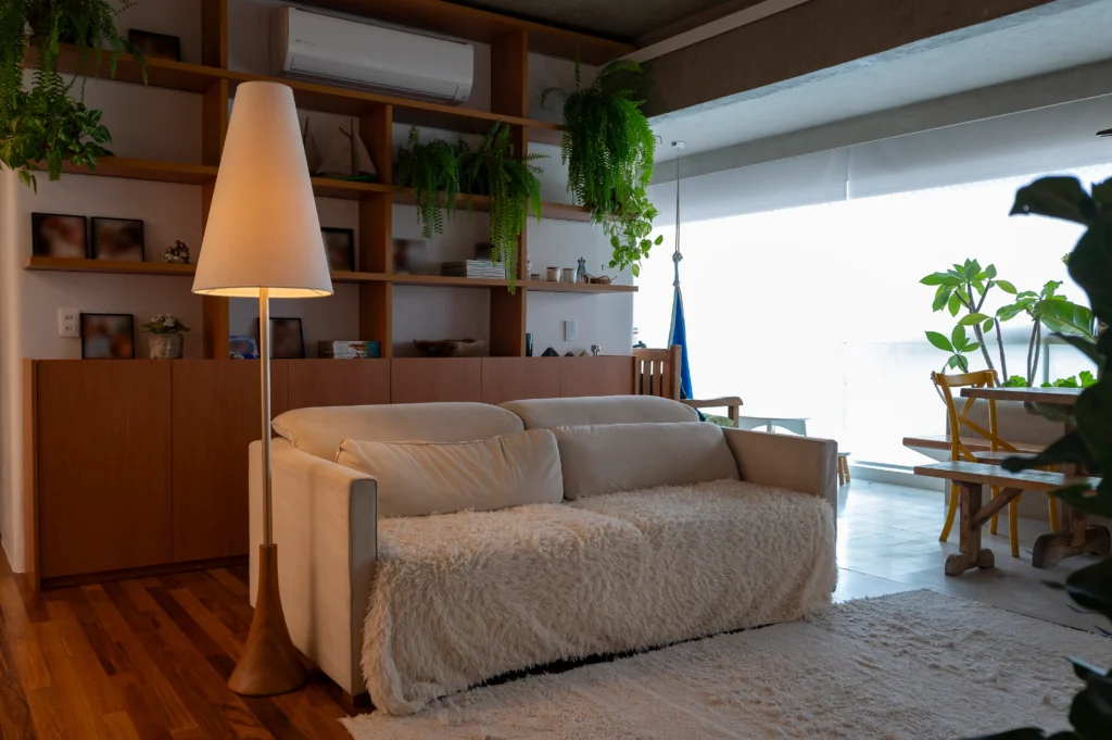 <img src="sala-de-estar-moderna-com-plantas-e-iluminacao-suave-jpg.webp" alt="Sala de estar moderna com sofá branco, iluminação suave, prateleiras de madeira, muitas plantas verdes, janelas grandes e decoração aconchegante.">
