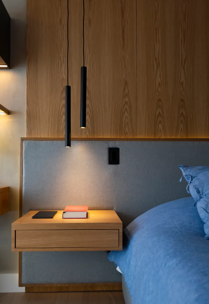 <img src="decoracaoquartoquedecoracaodecormoderna.webp" alt="Decoração de quarto com cabeceira de cama embutida em painel de madeira, iluminação moderna com pendentes pretos e mobiliário de design minimalista.">