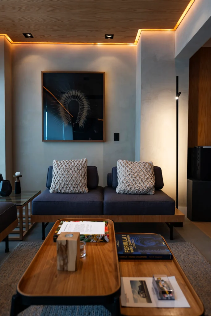 <img src="sala-de-estar-moderno-com-ator-fernando-monteiro.webp" alt="Imagem de uma sala de estar moderna com detalhes de iluminação embutida no teto, um quadro decorativo na parede, um sofá com almofadas decorativas, mesa de centro de madeira, e iluminação sutil criando um ambiente aconchegante.">