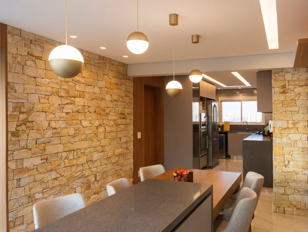 <img src="cozinha-moderna-com-parede-de-pedra.webp" alt="Imagem de uma cozinha moderna com paredes de pedra, iluminação pendente e mobiliário contemporâneo, criando um ambiente acolhedor e elegante.">