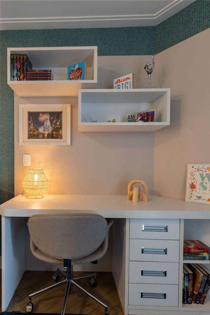Um espaço aconchegante, com uma mesa branca e livros organizados na lateral, um abajur de mesa com luz suave iluminando a mesa, criando uma atmosfera acolhedora. A cadeira confortável e as prateleiras ao fundo completam o ambiente perfeito para leitura e relaxamento.