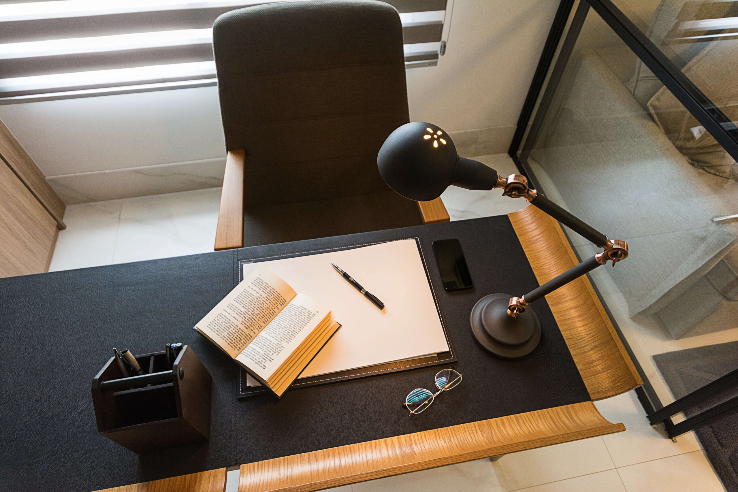 Um ambiente acolhedor para leitura, com mesa organizada, livro aberto, caneta e óculos, além de uma luminária direcionável com luz suave, criando um espaço perfeito para relaxar e ler durante as férias.