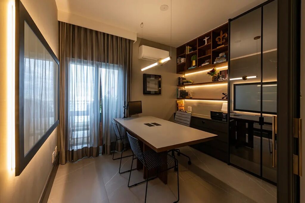 Ambiente de escritório moderno com mesa de trabalho, cadeiras, armário com iluminação, computador, lareira elétrica e cortinas de tecido cinza, ideal para home office com decoração contemporânea.