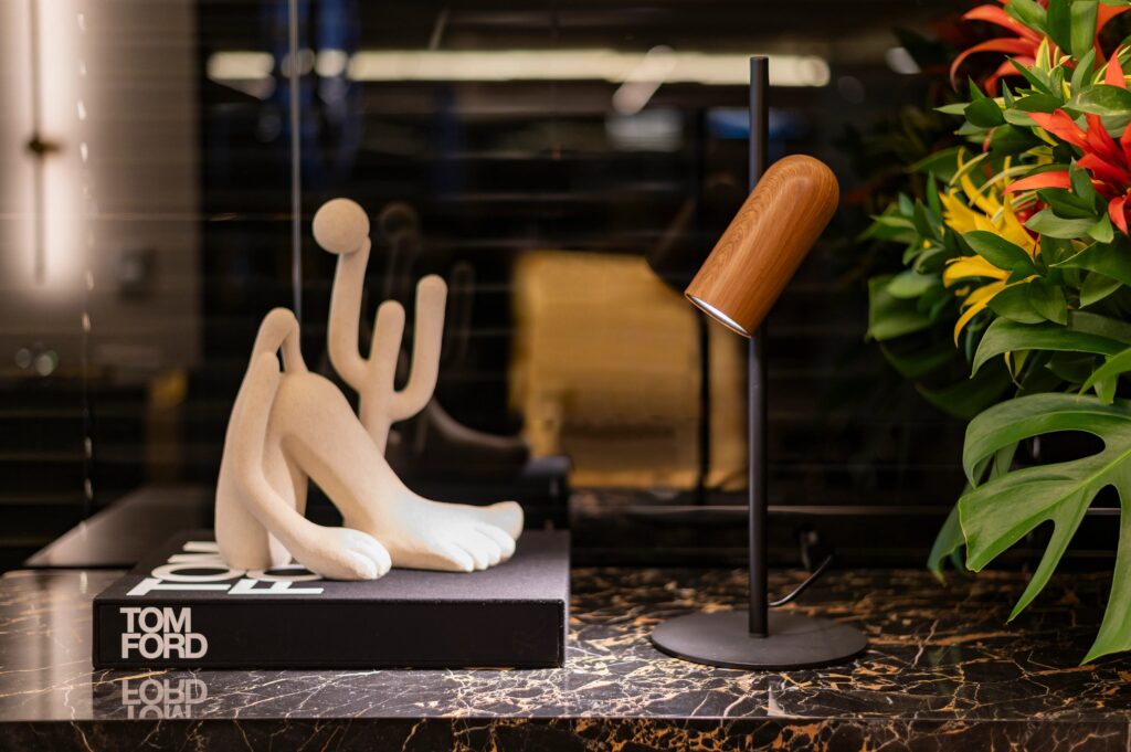 Decoração moderna com estatueta de cachorro estilizado, lâmpada de mesa e plantas verdes em ambiente de escritório ou living, destacando design contemporâneo e estilo minimalista.