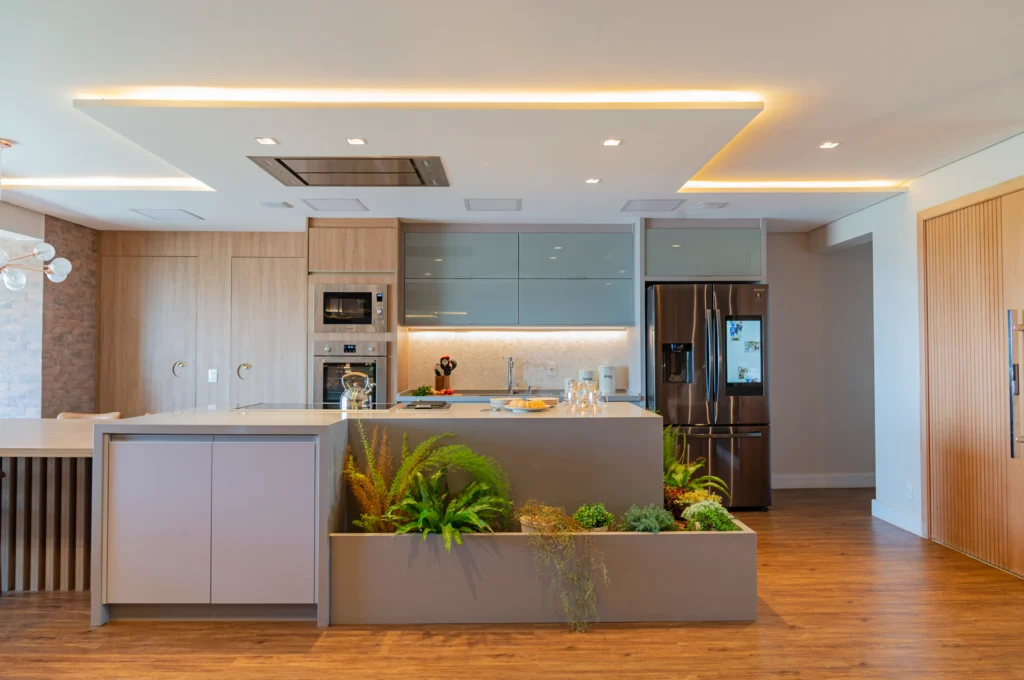Cozinha moderna com iluminação indireta em LED no forro, luminárias embutidas e ilha central com jardim decorativo.